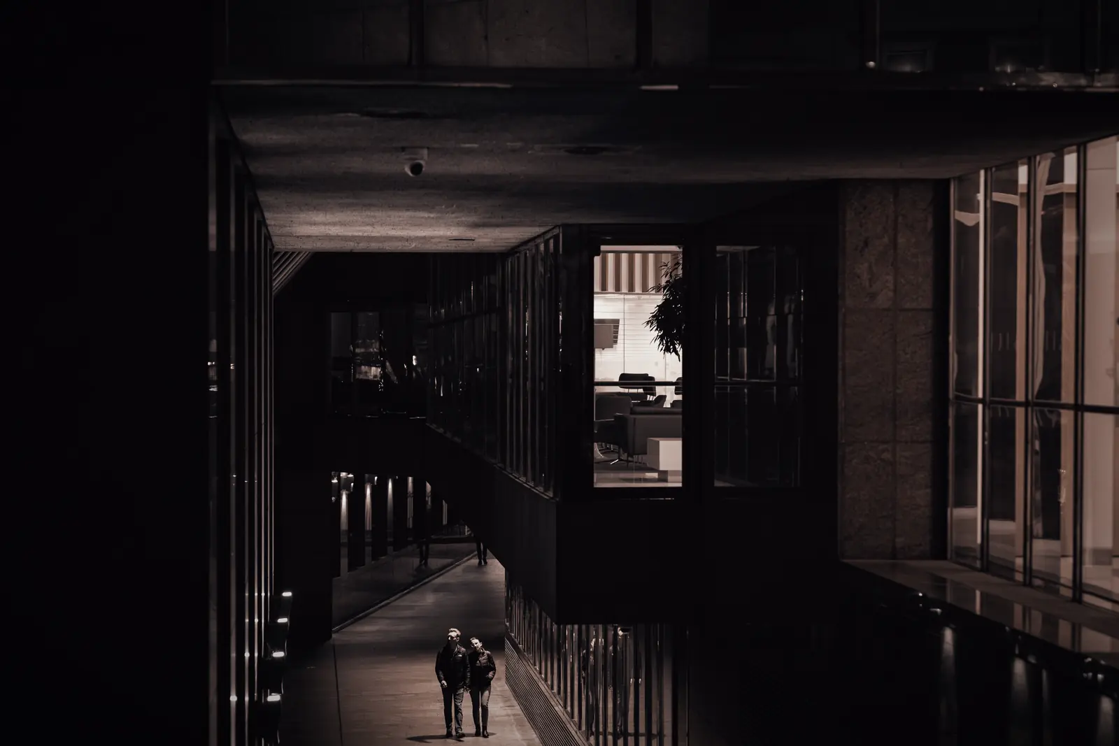 Two figures crossing a darkened architectural corridor